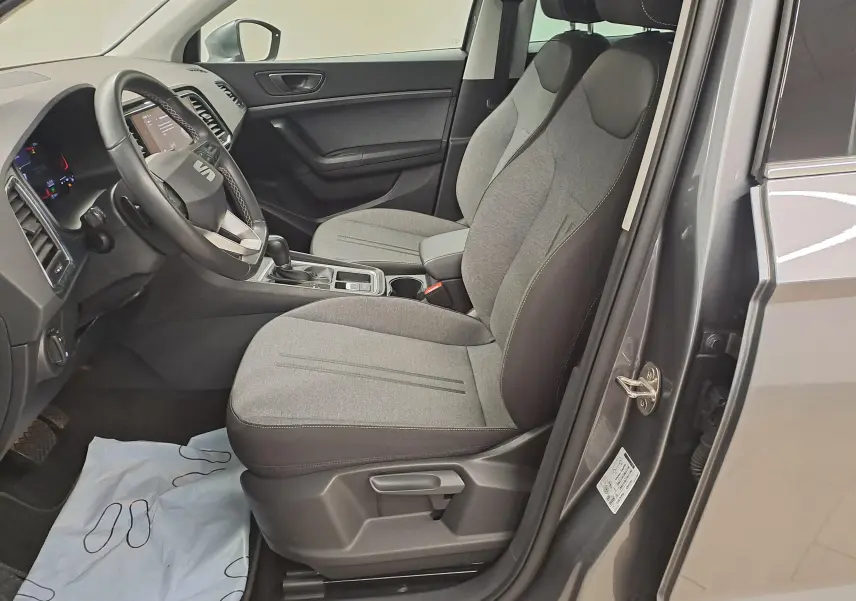 Vue intérieure côté conducteur du SEAT Ateca 2023 gris graphite, montrant sièges tissu gris et tableau de bord moderne.
