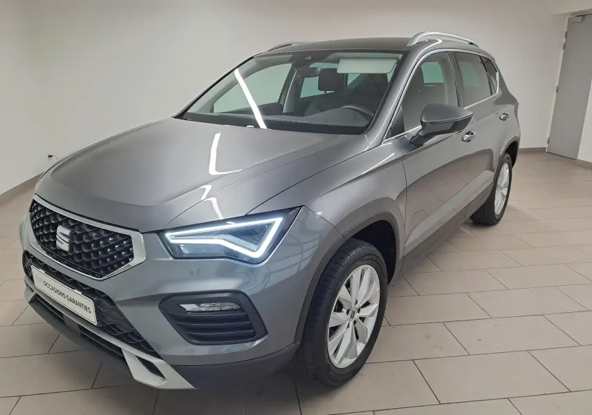 SEAT Ateca 2023 gris graphite en 3/4 avant droit, avec phares LED allumés et jantes argentées.