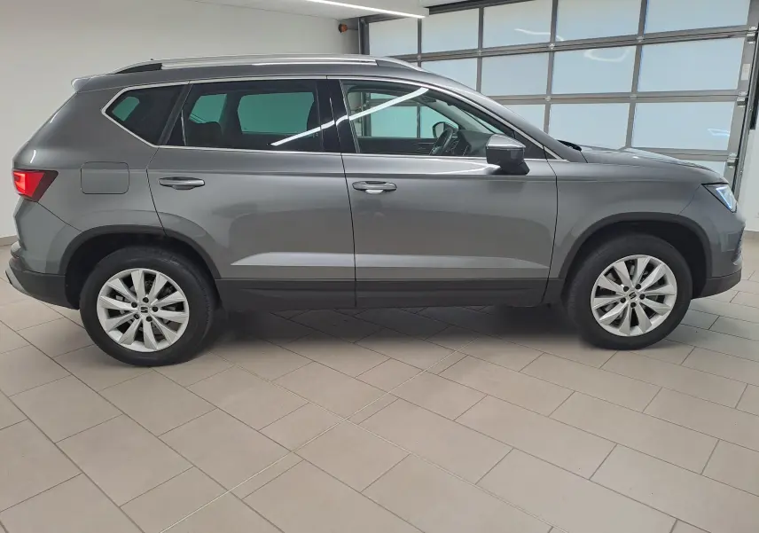 Vue de profil côté gauche d’un SEAT Ateca 2023 gris graphite avec jantes alliage et toit ouvrant en intérieur lumineux.