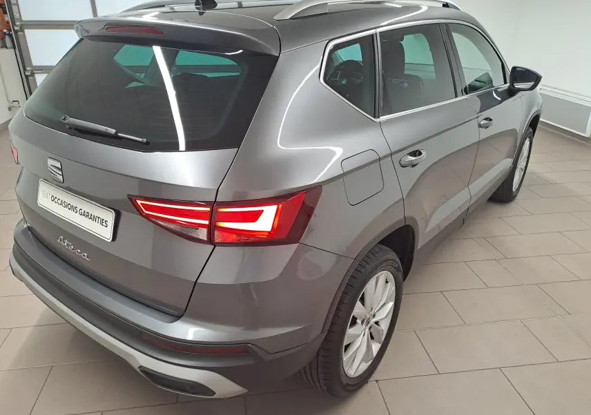 Vue 3/4 arrière droite d'un SEAT Ateca gris graphite métallisé, avec feux arrière allumés dans un showroom intérieur.