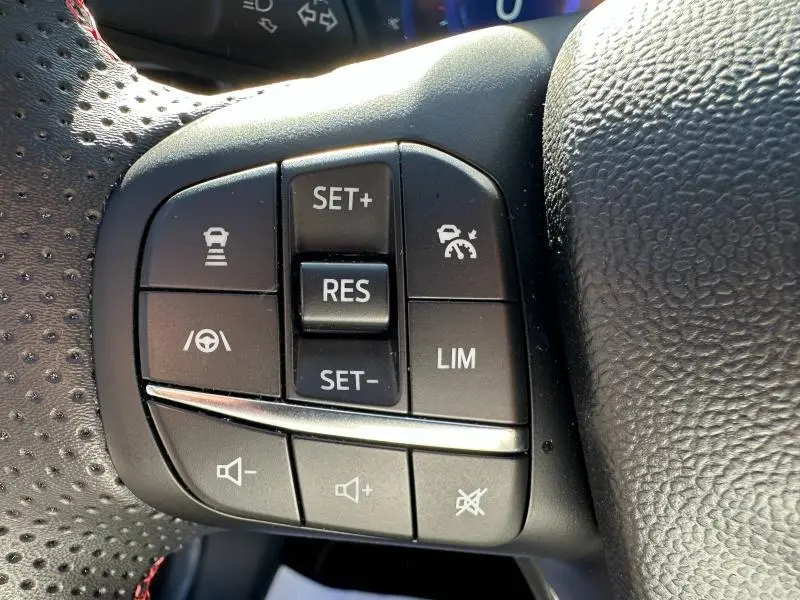 Gros plan sur les commandes au volant noir du Ford Puma 2023, avec boutons de régulateur de vitesse et volume sonore.