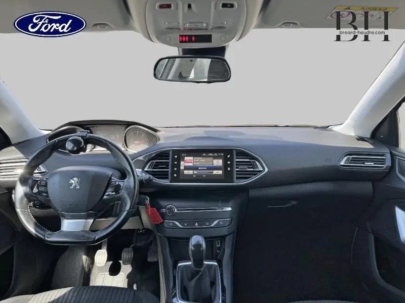 Vue intérieure avant du tableau de bord et volant cuir noir d'une Peugeot 308 gris Artense de 2016 avec écran tactile central.
