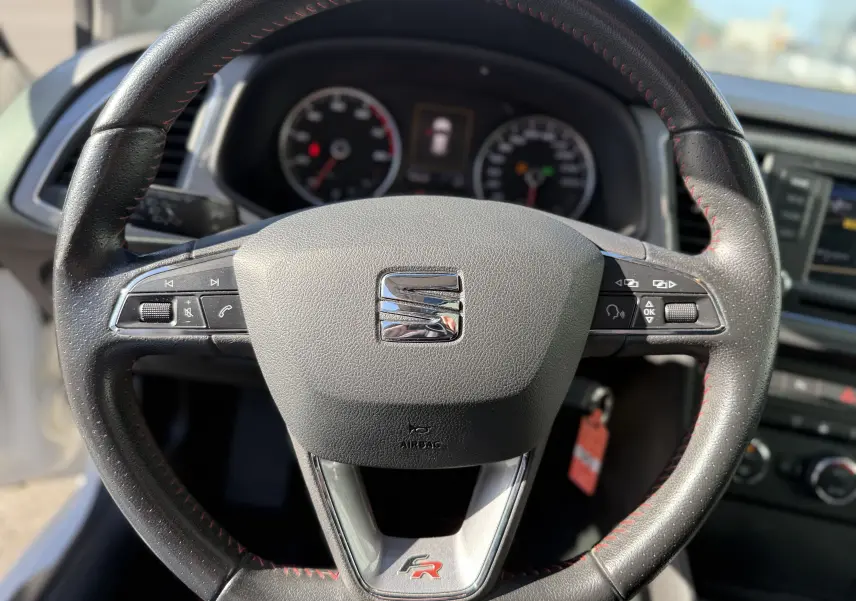Vue rapprochée du volant noir avec surpiqûres rouges du SEAT LEON 1.8 TFSI 180 FR, mettant en valeur le logo FR et les commandes intégrées.
