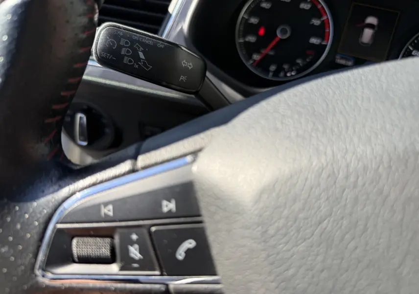 Détail du volant côté gauche avec commandes audio et levier de clignotant, tableau de bord partiellement visible d'une SEAT Leon blanche.