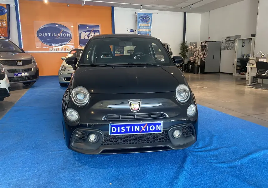 Vue frontale d'une ABARTH 595 noire avec logo distinctif et plaque "DISTINXION" en concession lumineuse.