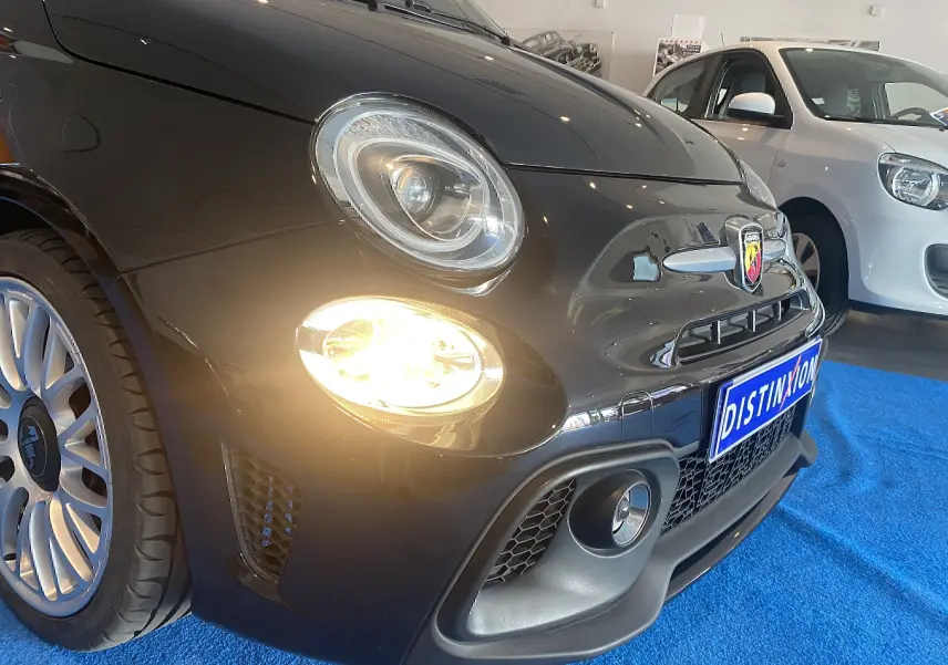 Vue 3/4 avant gauche d'une ABARTH 595 noire avec phares allumés et jantes alliage 17 pouces en showroom.