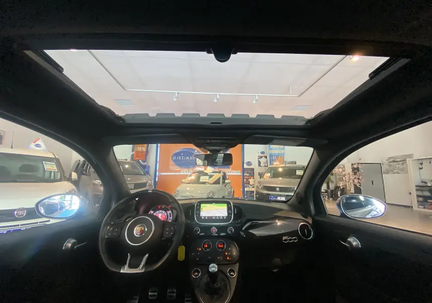 Vue intérieure du toit ouvrant électrique et tableau de bord noir de l'Abarth 595 avec écran GPS allumé.