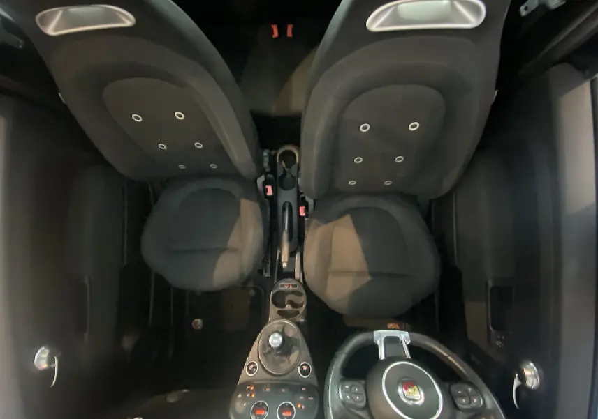 Vue intérieure plongeante de l'habitacle noir de l'Abarth 595 avec volant à droite et sièges avant en tissu.