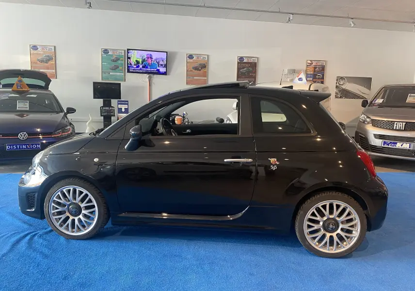 Profil côté gauche d'une ABARTH 595 noire avec jantes alliage et toit ouvrant visible en intérieur showroom.