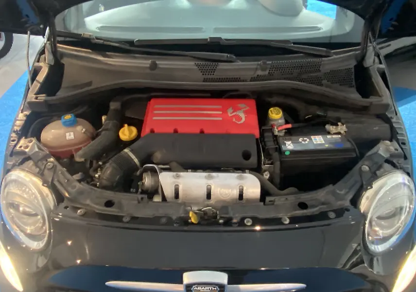 Moteur rouge visible sous le capot ouvert d'une ABARTH 595 noire vue de face, avec phares ronds allumés.