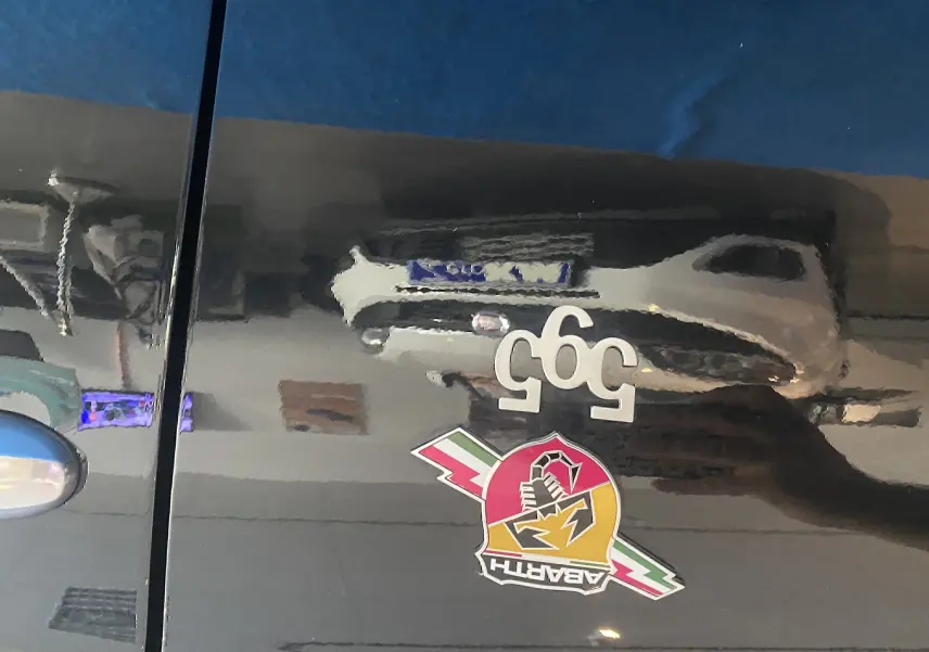 Gros plan sur la porte noire d'une Abarth 595 avec logo scorpion coloré et badge 595 blanc.