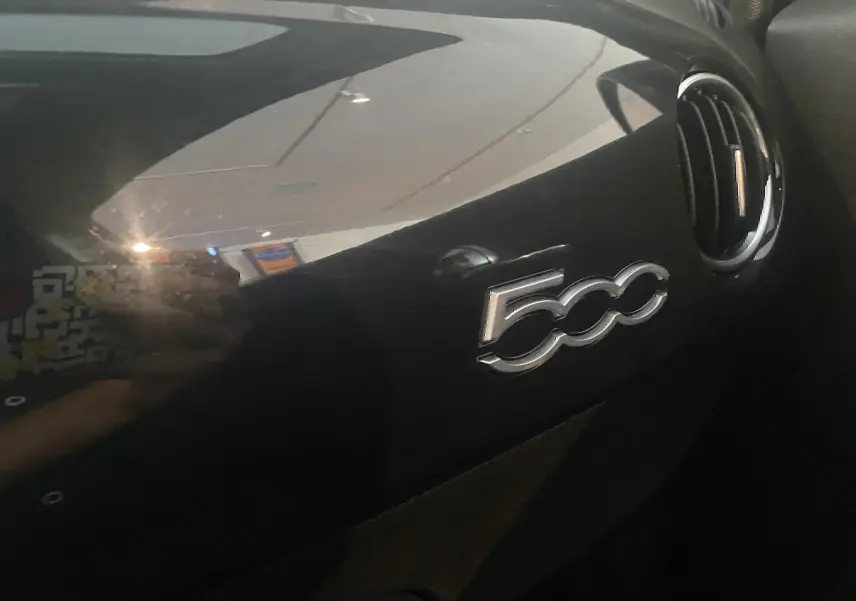 Gros plan sur le tableau de bord noir brillant de l'Abarth 595 avec le logo "500" et une sortie d'air ronde à droite.
