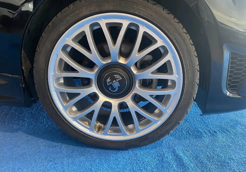 Gros plan sur la jante alu 17 pouces argentée avec logo Abarth au centre, sur roue avant droite d'une ABARTH 595 noire.