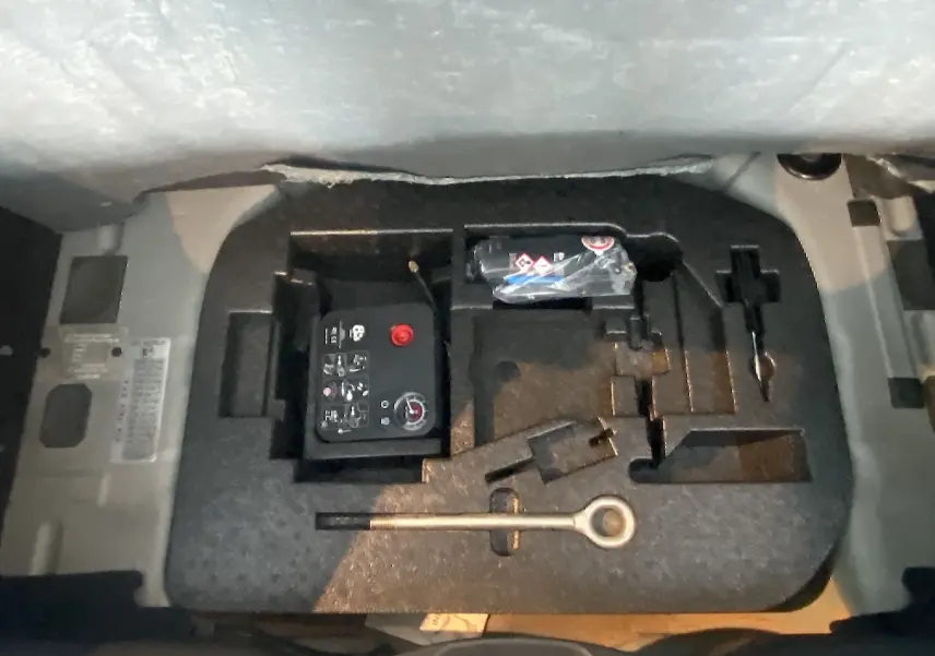 Gros plan sur le compartiment à outils et kit de réparation sous le coffre de l'Abarth 595 noir de 2018.