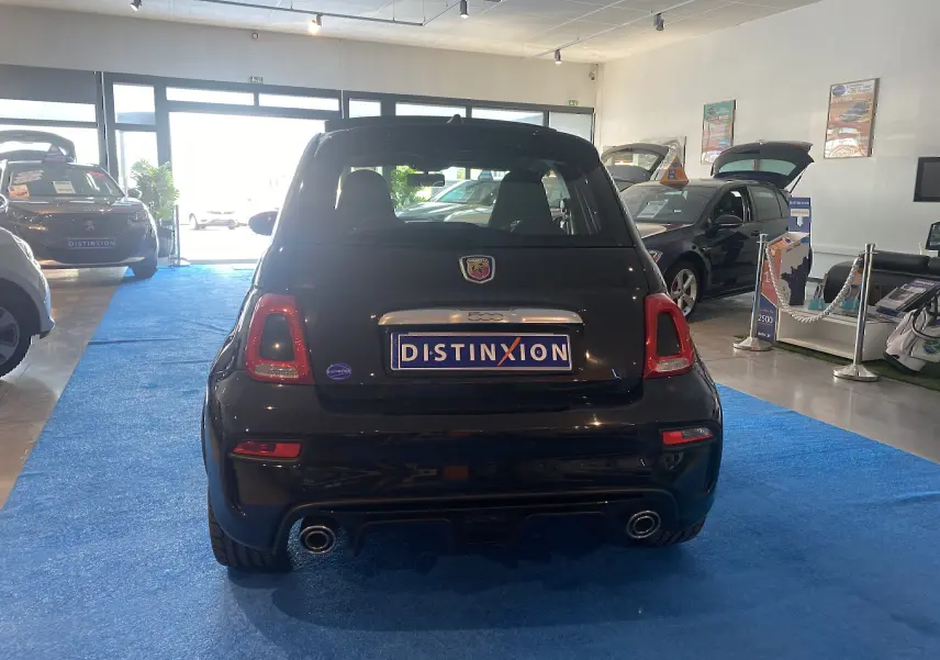 Vue arrière d'une ABARTH 595 noire exposée en showroom avec double sortie d'échappement et toit ouvrant visible.