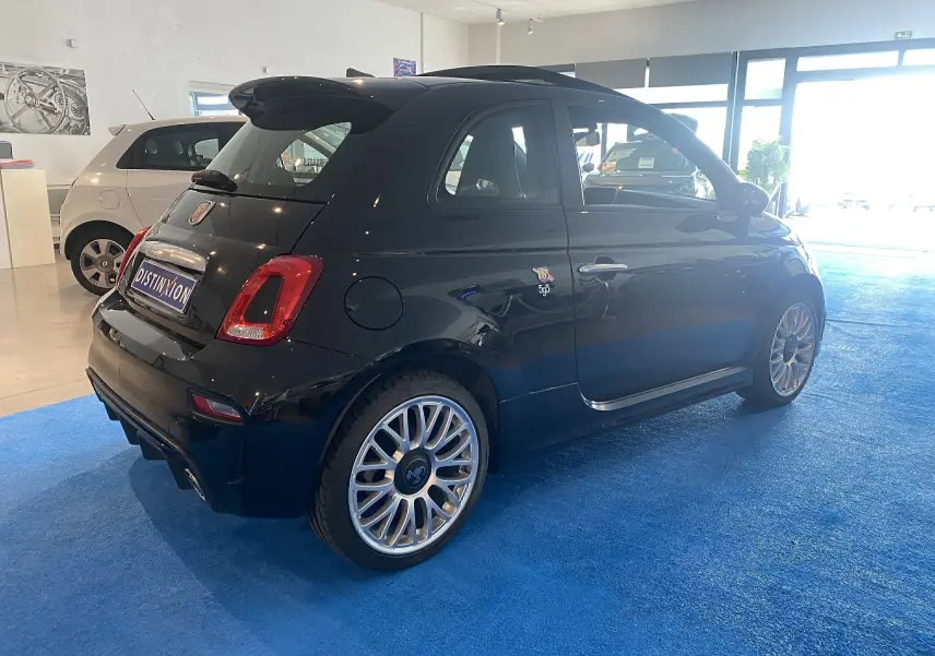 ABARTH 595 noir en vue 3/4 arrière droit, avec jantes alu 17 pouces et toit ouvrant électrique visible en intérieur showroom.