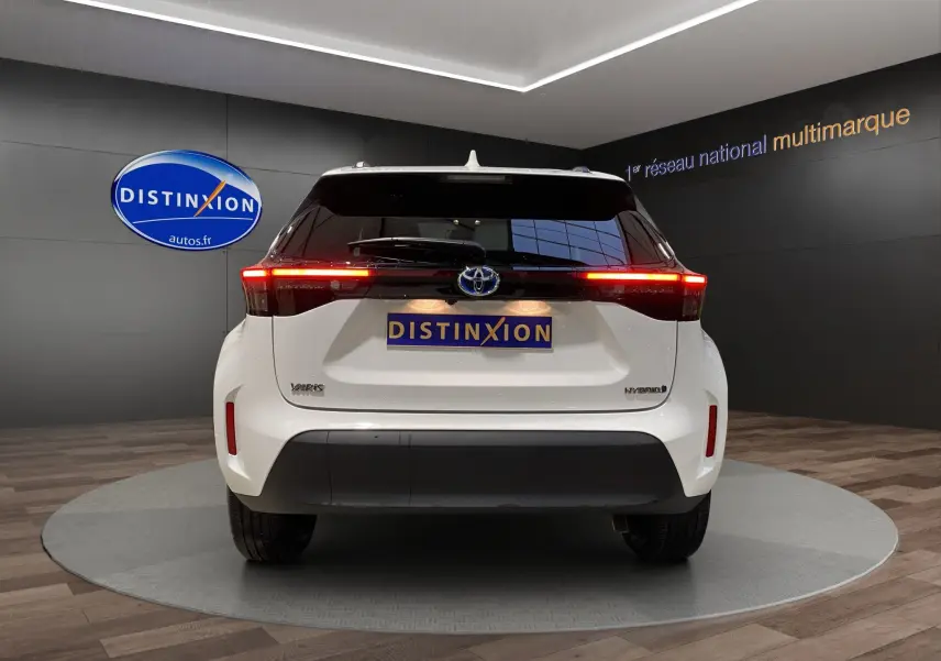 Vue arrière d'une Toyota Yaris Cross blanche hybride avec feux LED allumés dans un showroom.