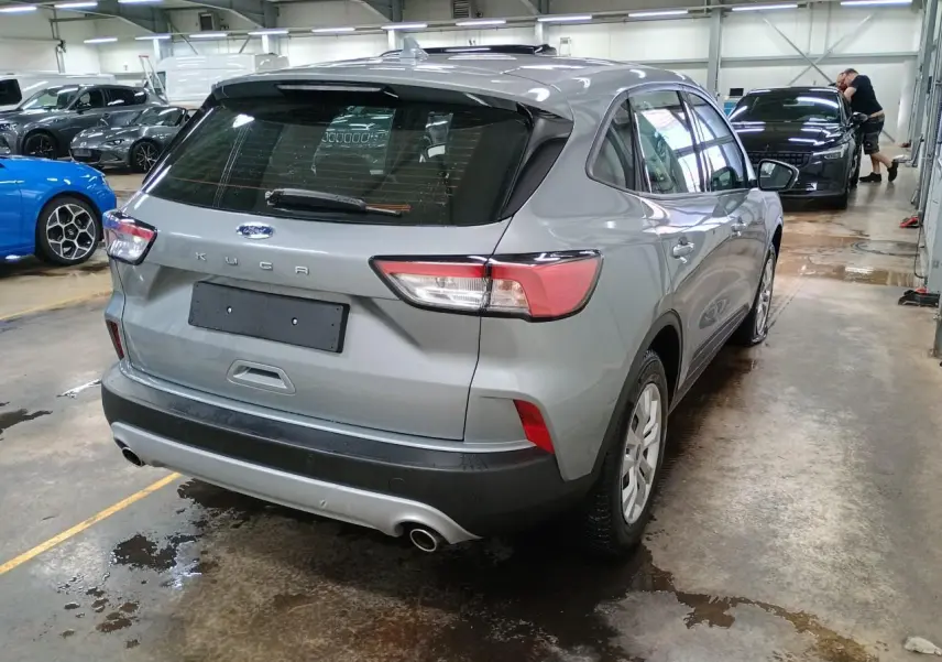Vue 3/4 arrière droite d'un Ford Kuga 2024 gris Solar dans un garage, avec feux arrière et double sortie d'échappement visibles.