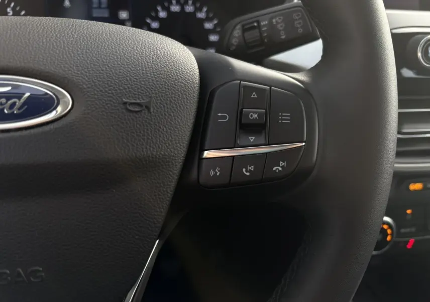 Gros plan sur le volant multifonctions en cuir du Ford Kuga 2024, montrant les commandes à droite et le logo Ford central.