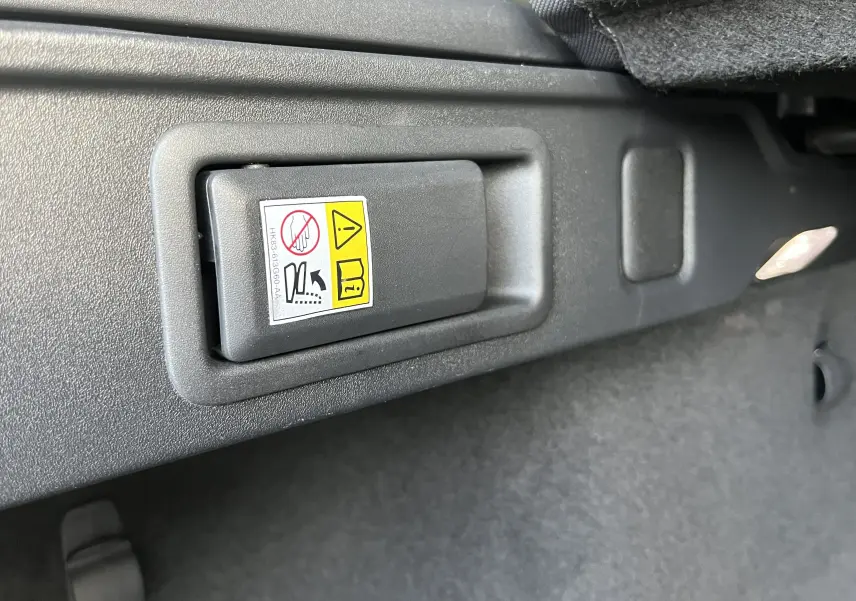 Détail intérieur du coffre du Jaguar F-PACE blanc 2018, montrant la poignée de déverrouillage d'urgence.