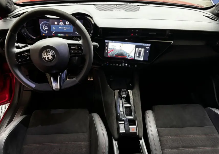 Vue intérieure avant de l'Alfa Romeo Junior 2024, volant cuir, écran tactile central affichant l'aide au stationnement.