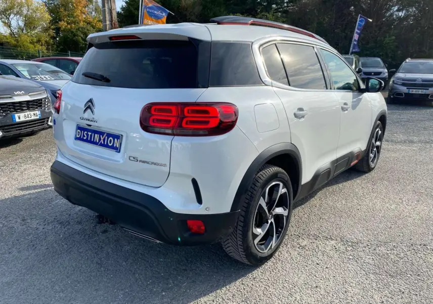 Vue 3/4 arrière droite d'un Citroën C5 Aircross blanc avec jantes bi-ton et inserts rouges distinctifs.