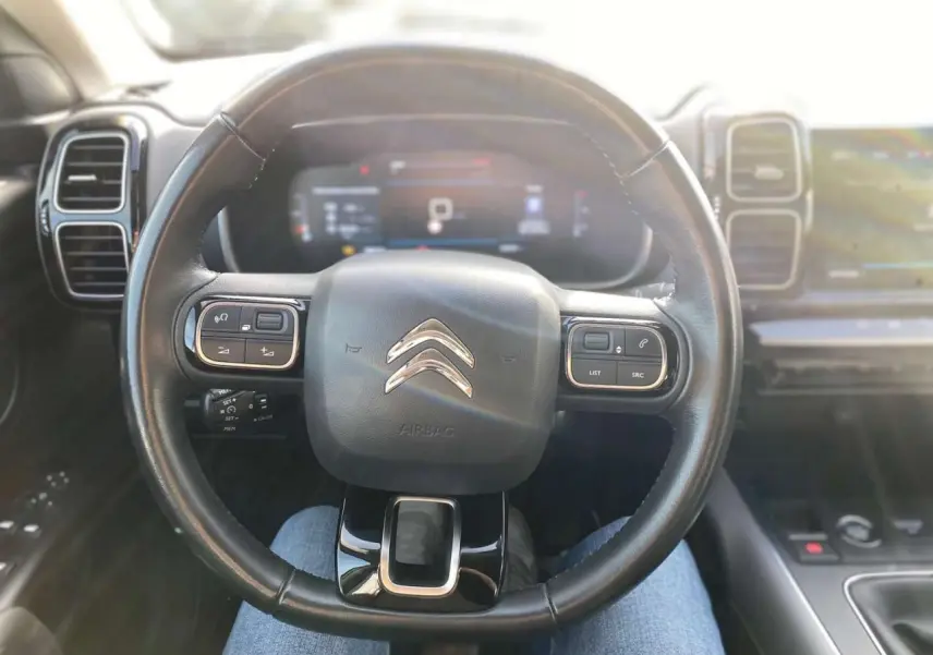 Vue intérieure centrée sur le volant cuir noir de la Citroën C5 Aircross 2021 avec tableau de bord numérique flou en arrière-plan.