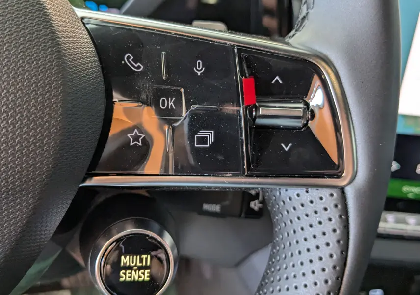 Gros plan sur les commandes au volant côté gauche du Renault Austral blanc nacré, avec bouton Multi Sense éclairé.