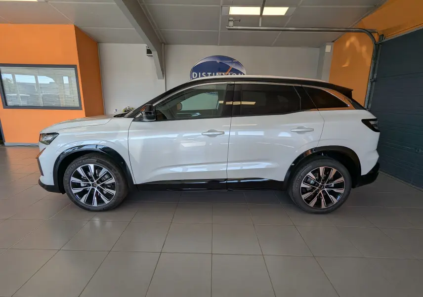 Profil droit du Renault Austral blanc nacré avec toit noir, jantes alliage 19 pouces, en intérieur showroom.