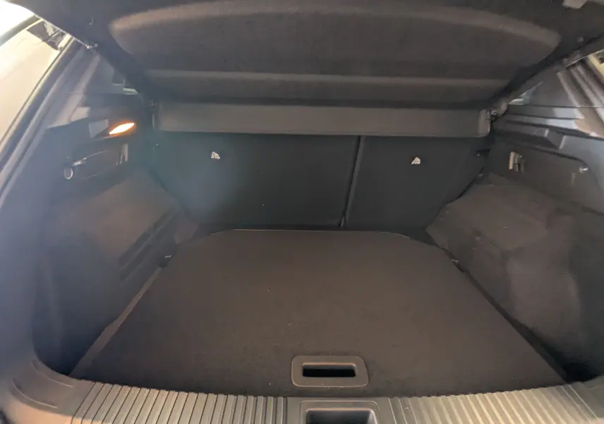 Coffre ouvert vu de l'arrière du Renault Austral E-Tech blanc nacré avec intérieur noir et cache-bagages déployé.