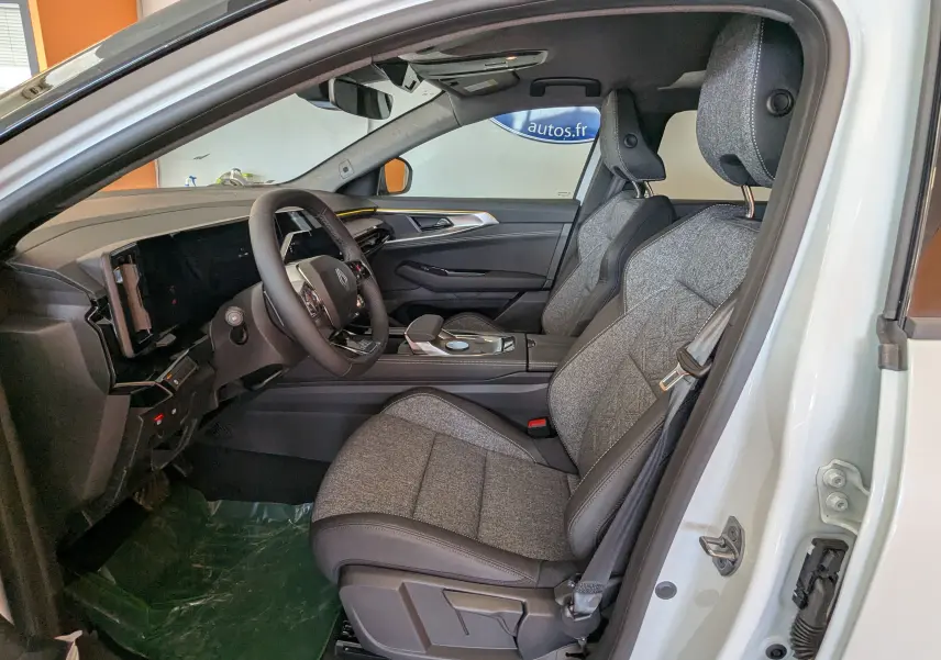 Vue intérieure côté conducteur du Renault Austral E-Tech blanc nacré, sièges tissu gris nuancé et tableau de bord moderne.