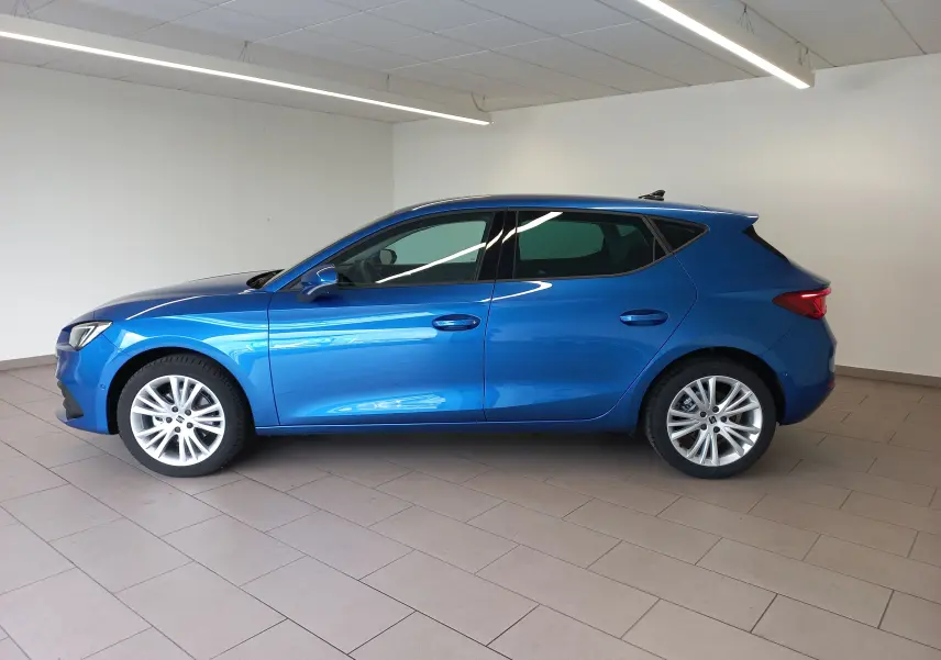 Vue de profil côté gauche d'une SEAT Leon 2025 bleu saphir aux vitres arrière surteintées dans un intérieur lumineux.