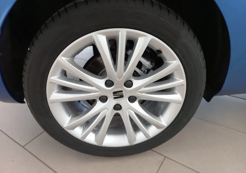 Gros plan sur la jante alliage argentée de la SEAT LEON 1.5 eTSI Bleu Saphir, avec partie de la carrosserie visible en arrière-plan.