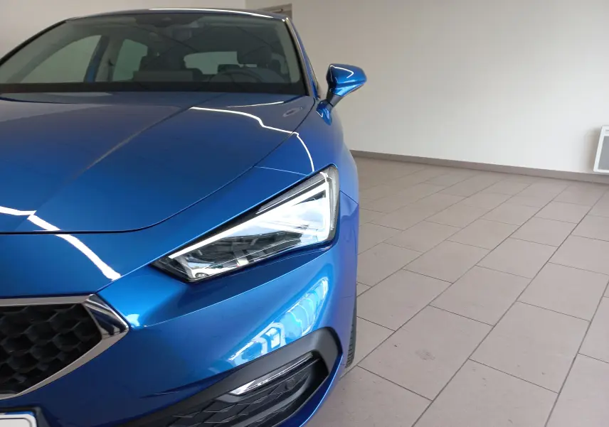 Vue rapprochée 3/4 avant droit d'une SEAT LEON 2025 bleu saphir avec phare LED et rétroviseur électrique.