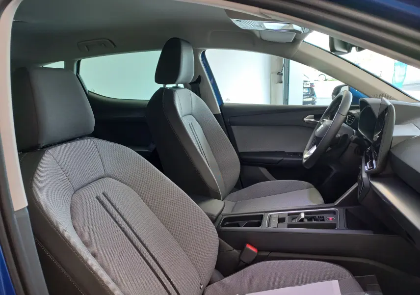Vue intérieure côté conducteur du SEAT Leon 2025, sièges gris et tableau de bord moderne avec écran tactile.