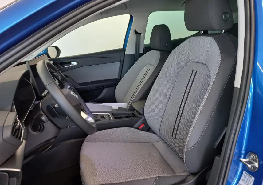 Vue intérieure côté conducteur de la SEAT LEON 2025 bleu saphir, montrant les sièges gris et le volant moderne.