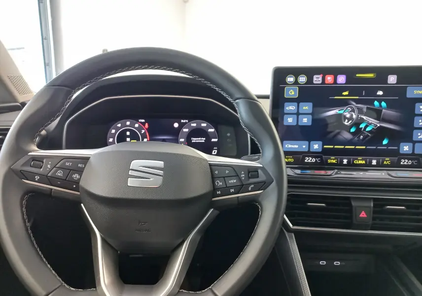 Vue intérieure centrée sur le volant noir de la SEAT LEON 1.5 eTSI 115 DSG7 avec écran tactile 12,9 pouces allumé.