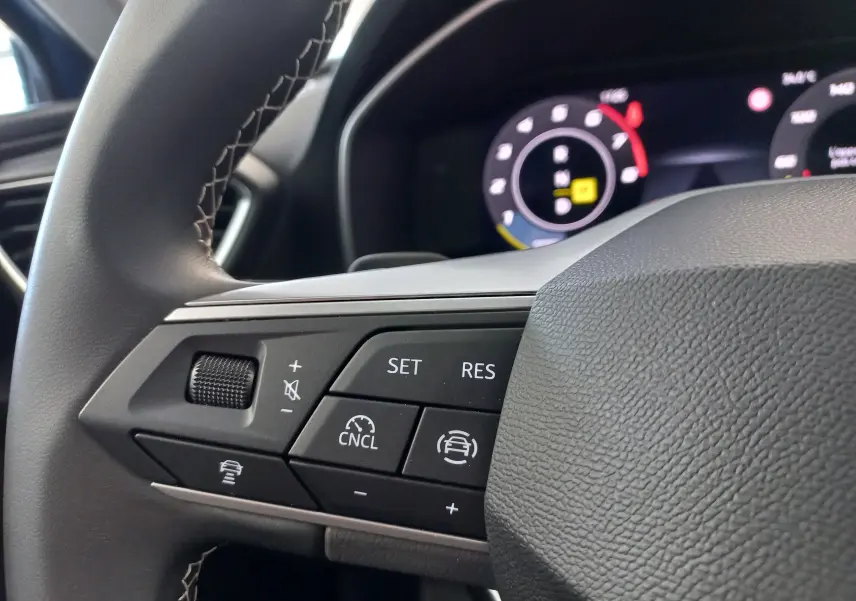 Gros plan sur les commandes du volant côté gauche du SEAT Leon 1.5 eTSI 115 DSG7, avec affichage numérique en arrière-plan.