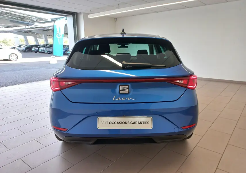 Vue arrière d'une SEAT Leon 2025 bleu saphir, avec feux arrière LED reliés et plaque "Occasions garanties".