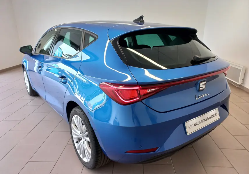Vue 3/4 arrière gauche d'une SEAT Leon 2025 bleu saphir avec vitres arrière surteintées et rétroviseurs rabattables.
