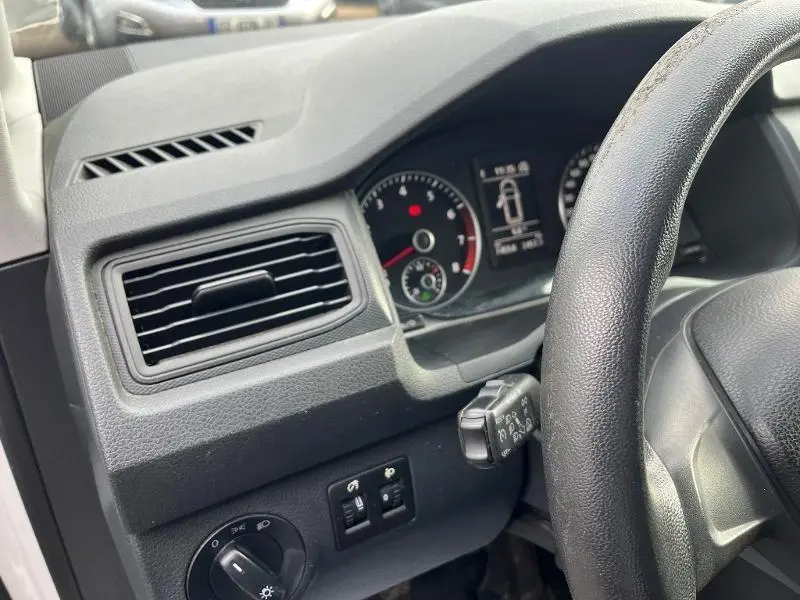 Détail du tableau de bord noir et volant côté gauche du Volkswagen Caddy Van blanc Candy 2016 en intérieur.