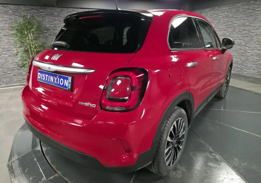 Fiat 500X rouge vue 3/4 arrière droit, avec toit noir et jantes alliage 17 pouces dans un showroom.