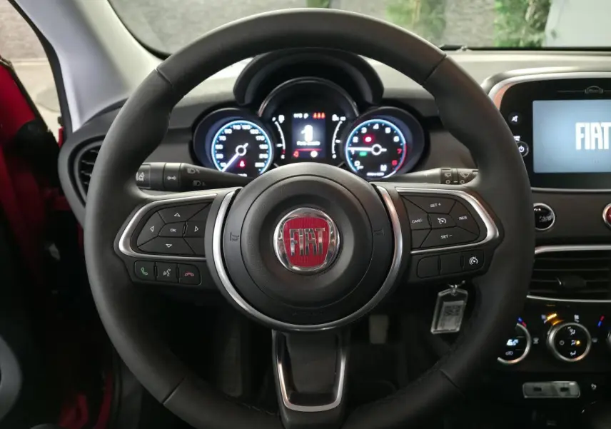 Vue centrée sur le volant noir du Fiat 500X 2024 avec tableau de bord et écran multimédia allumé.