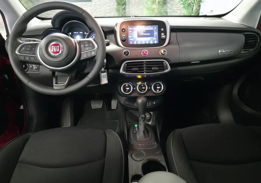 Vue intérieure frontale de la Fiat 500X 2024 avec tableau de bord gris titane et volant multifonction noir.