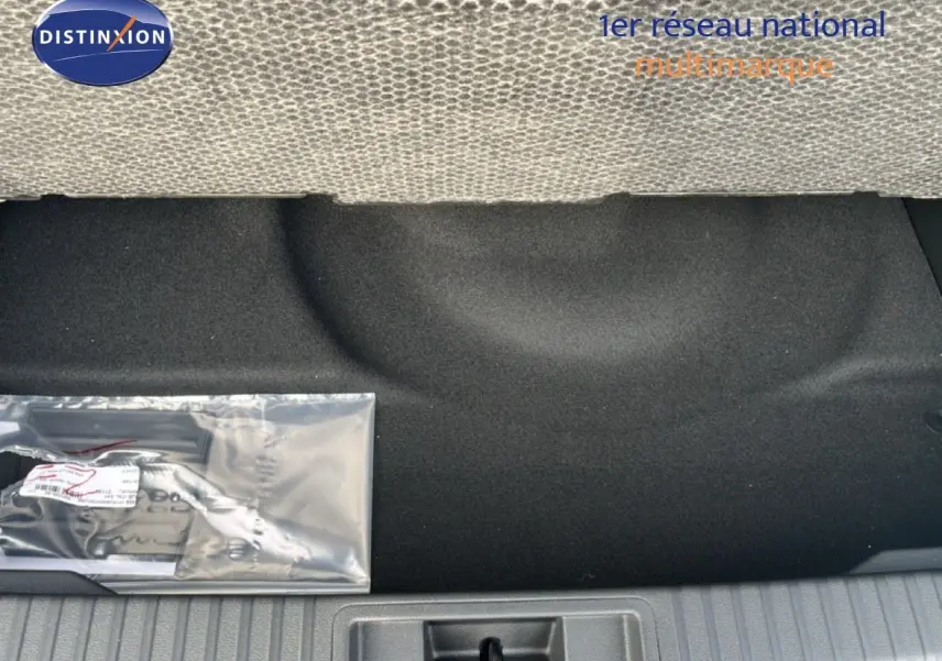 Vue du coffre arrière d'une Renault Symbioz blanc nacré, montrant le tapis noir et un kit d'accessoires emballé.