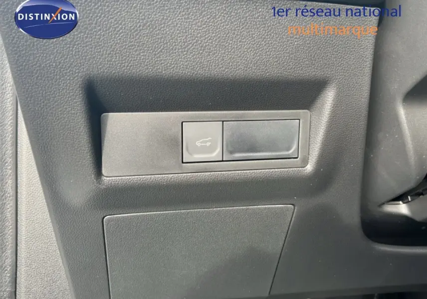 Détail du bouton d'ouverture du coffre sur la planche de bord noire d'une Renault Symbioz blanche nacrée.