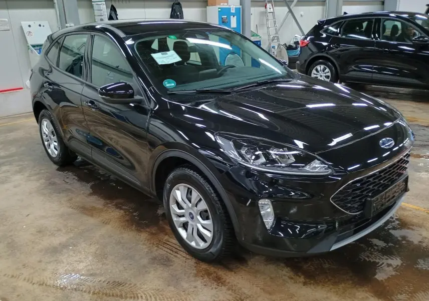 Ford Kuga noir Obsidien vu en 3/4 avant droit dans un garage, mettant en valeur sa calandre et ses phares modernes.