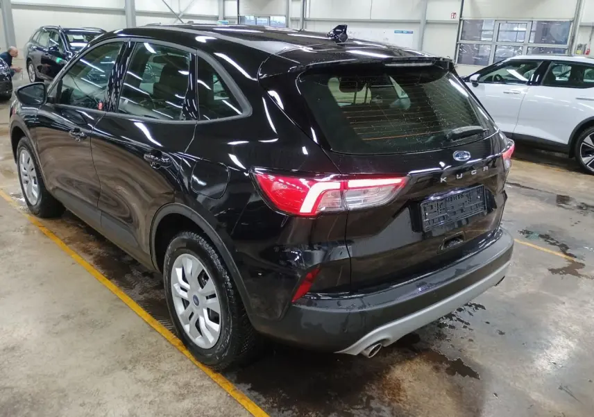 Vue 3/4 arrière droite d'un Ford Kuga noir Obsidien 2024 dans un garage, avec feux arrière allumés.