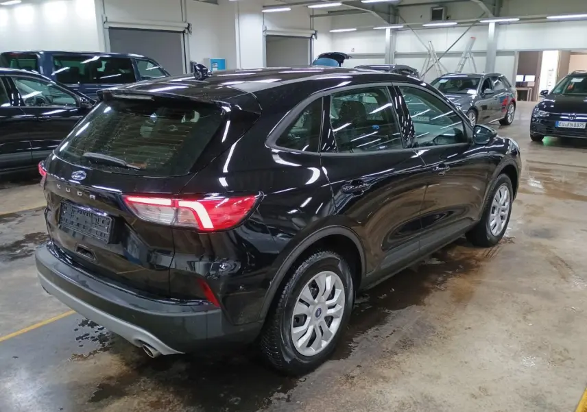 Ford Kuga noir Obsidien vu en 3/4 arrière droit dans un garage avec feux arrière allumés.