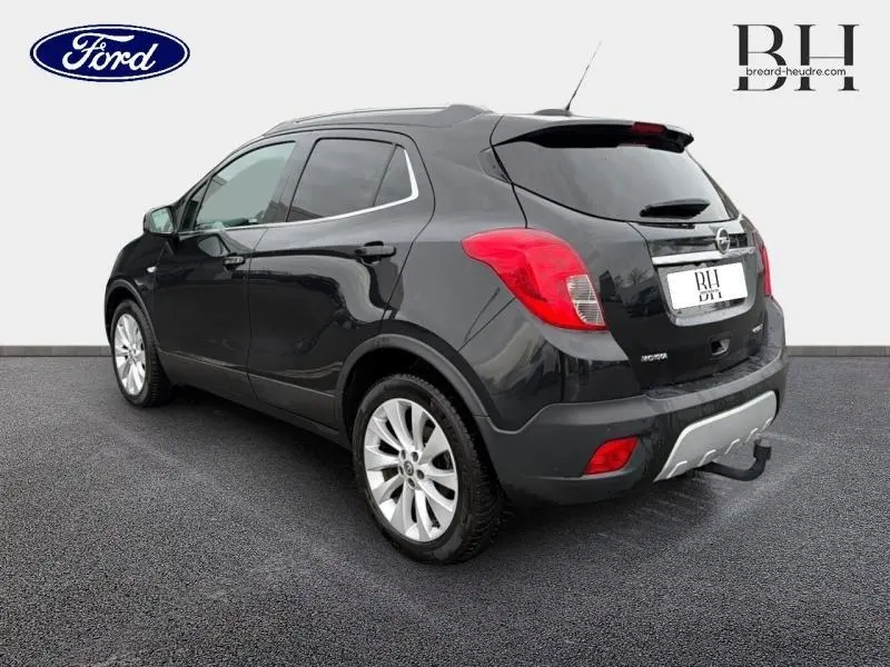 Vue 3/4 arrière droite d'un Opel Mokka noir carbone avec jantes alu et barres de toit visibles.